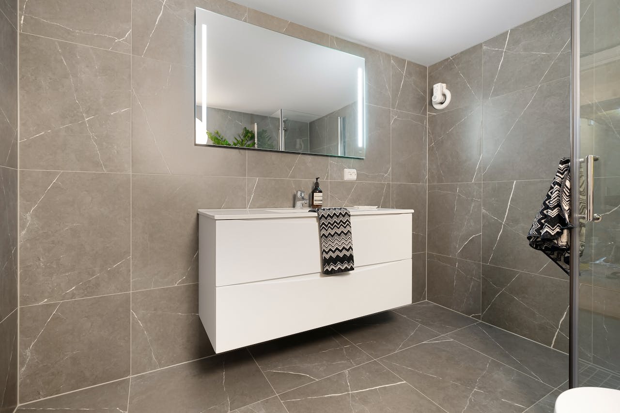 Home Elegant bathroom featuring a large mirror, modern vanity, and sleek grey tiled walls.