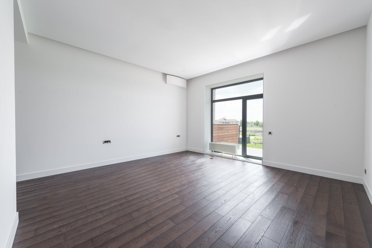 Home Bright and spacious modern room with a dark wooden floor and large window offering outdoor view.